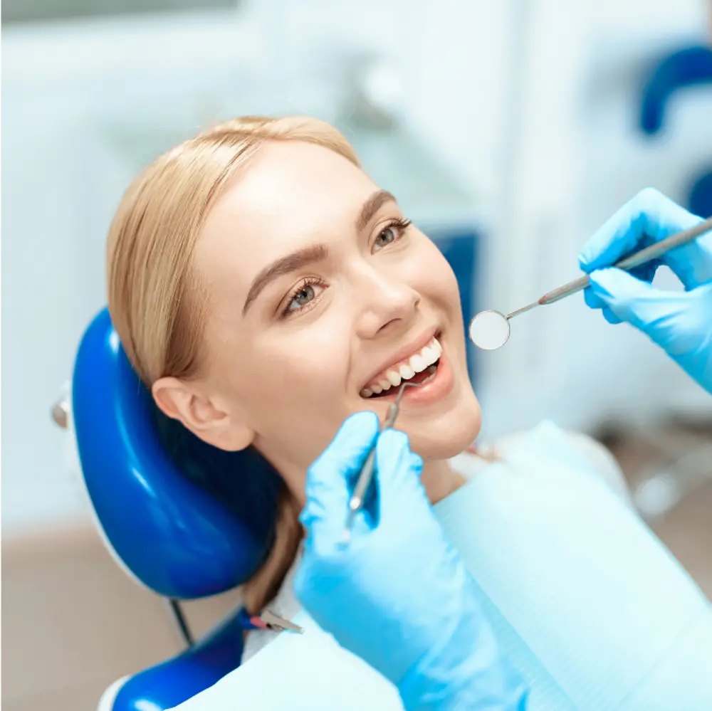 Woman at dentist's office receiving dental check-up, lying in a dental chair, smiling while a dentist examines her teeth with dental tools.