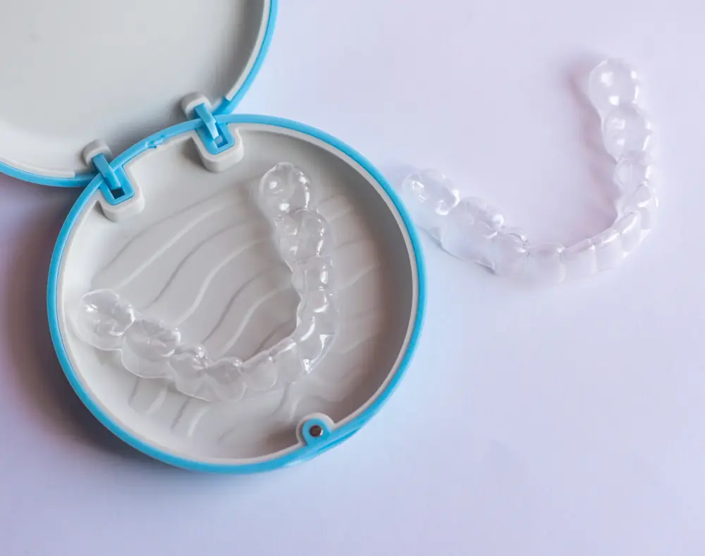 Clear dental aligners inside and outside a round, blue-and-white plastic case on a white surface.