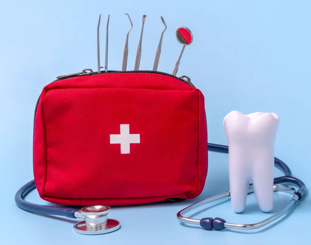 Red medical kit with dental tools, a white tooth model, and a stethoscope against a light blue background.