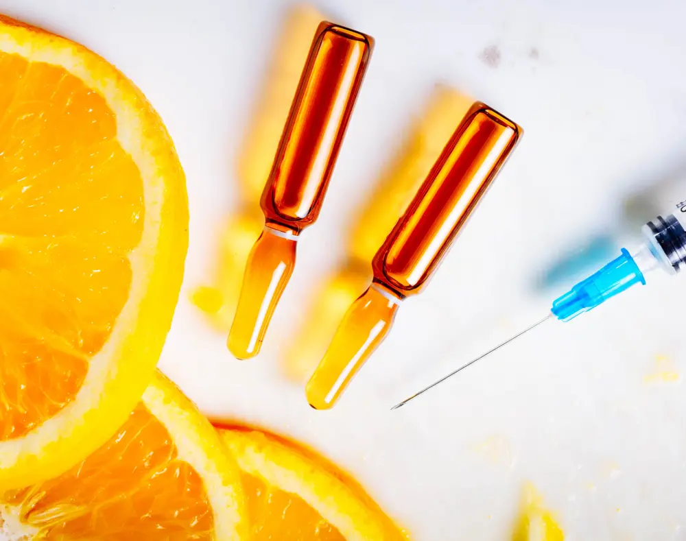 Vials of orange liquid and a syringe next to orange slices on a white surface.