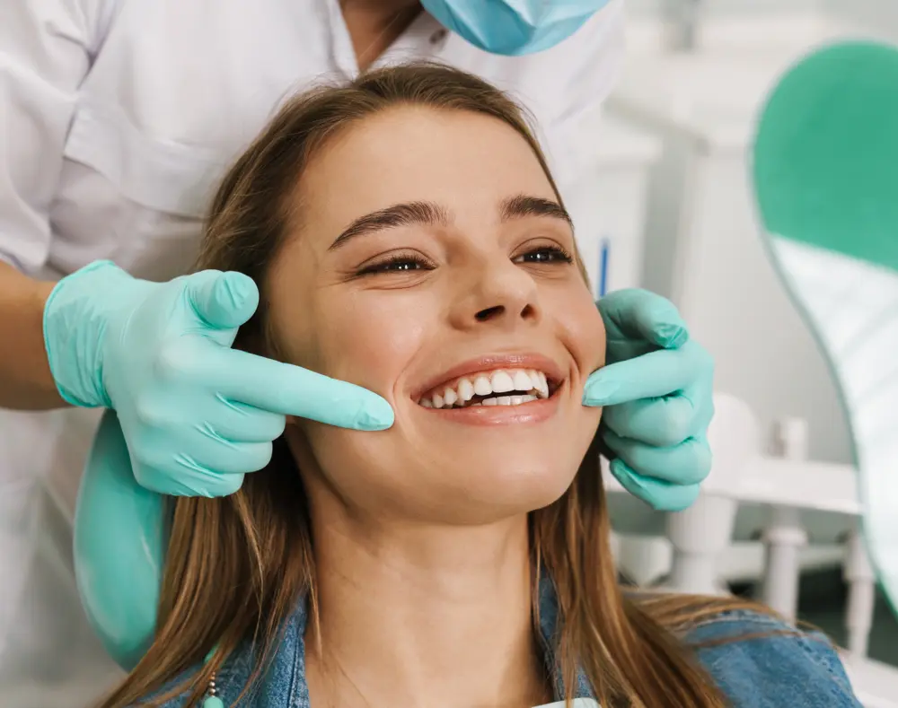 A woman smiling during a dental check-up, with a dentist using gloved hands to examine her teeth in a bright dental office.