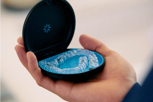 Hand holding an open case with clear dental aligners inside, against a blurred background.