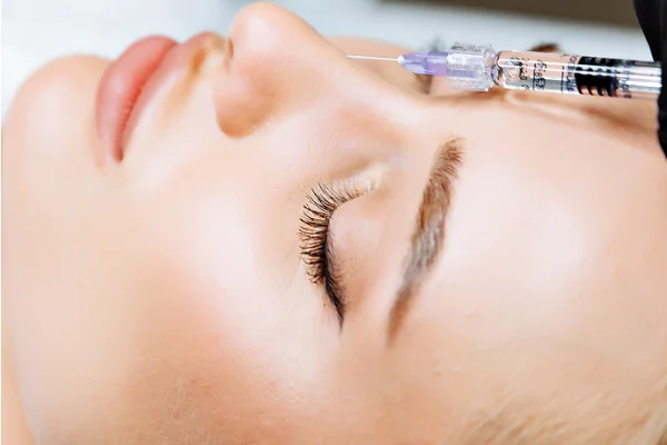 A person receiving a facial or cosmetic injection near the nose, close-up shot showing closed eyes and detailed skin texture.