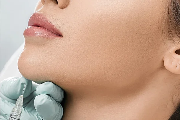 Close-up of a woman’s face receiving a cosmetic injection on her cheek, with a healthcare professional in gloves holding a syringe near her skin.