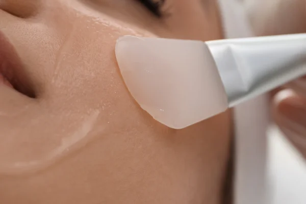 Close-up of a person receiving a facial treatment with a transparent gel or mask applied to their cheek area.