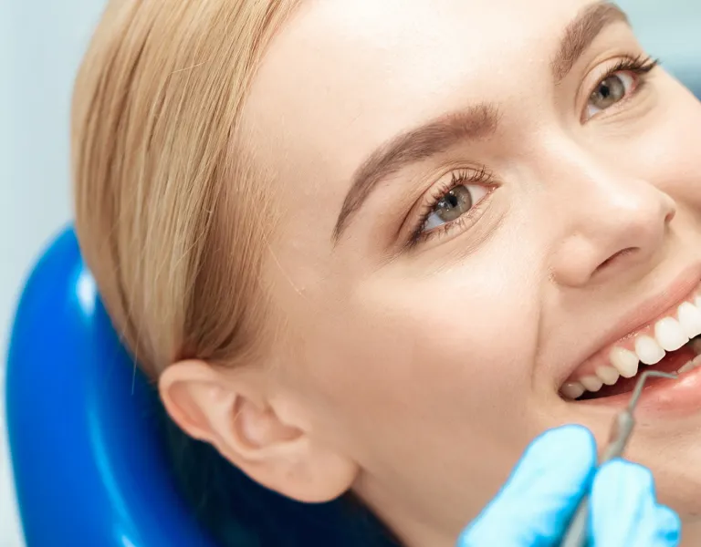 A woman smiling in a dental chair during a check-up, with a dentist using tools to examine her teeth.