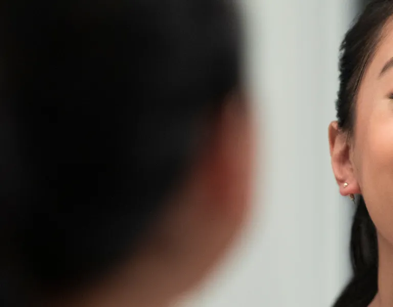 A woman with a bright smile and earrings looks into a mirror, reflecting her face with a blurred foreground of her head.