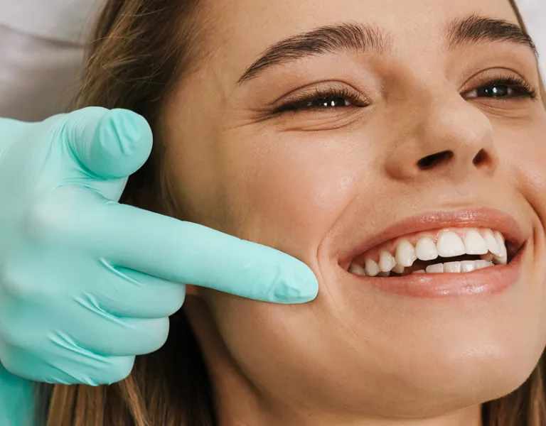 A woman with a bright smile receives dental care from a dentist wearing green gloves in a dental clinic.