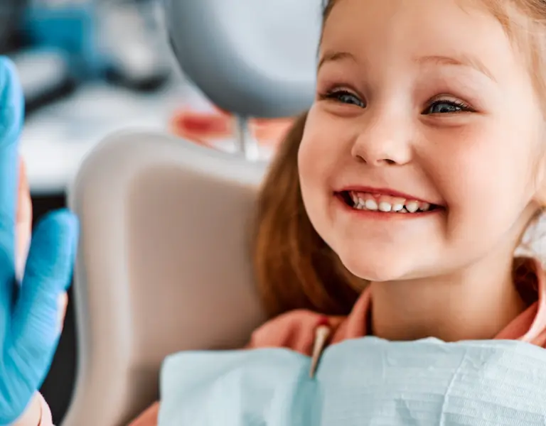 A young girl with red hair smiling happily at a dentist, showing her teeth during a dental check-up in a dental clinic.